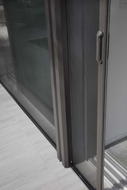 Detail of a sliding glass door frame and handle with fine mesh screen along a tiled threshold.