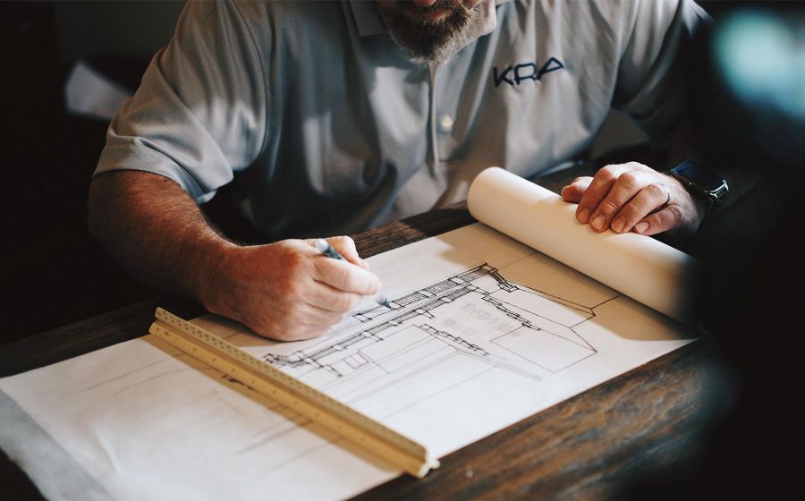 Close-up of a designer sketching architectural plans on a large blueprint with a ruler on the desk.