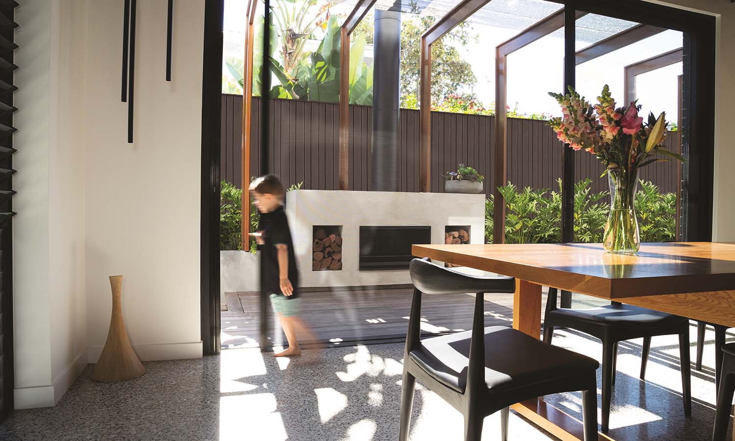 Child walking through an open sliding door to a sunny patio with an outdoor fireplace.
