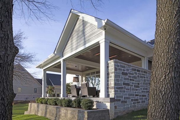 Enclosed porch with clear drop-down screens on a raised stone patio, outdoor dining set visible inside.