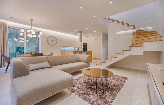 Bright modern open-plan living area with minimalist sofa, round coffee table, dining space, and a floating staircase.